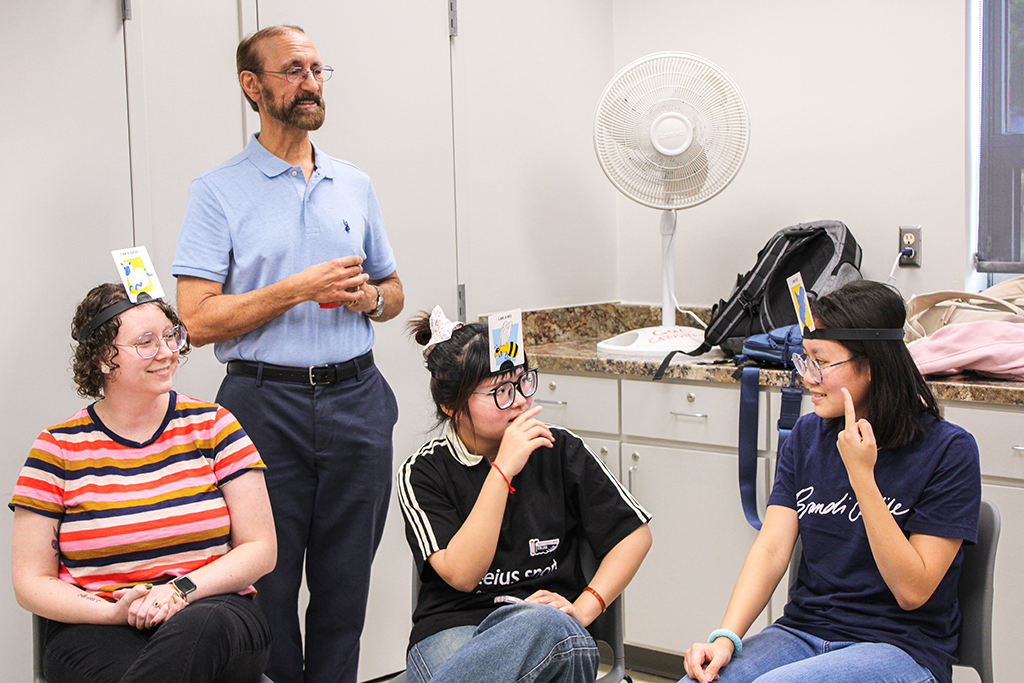 Students at a Conversation Partners meeting playing a game with picture cards on their heads.