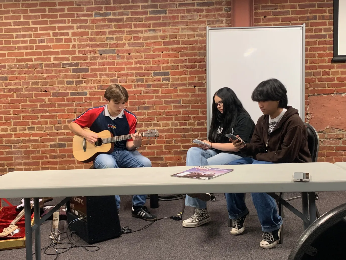 Three attendees seated by table, one playing the guitar